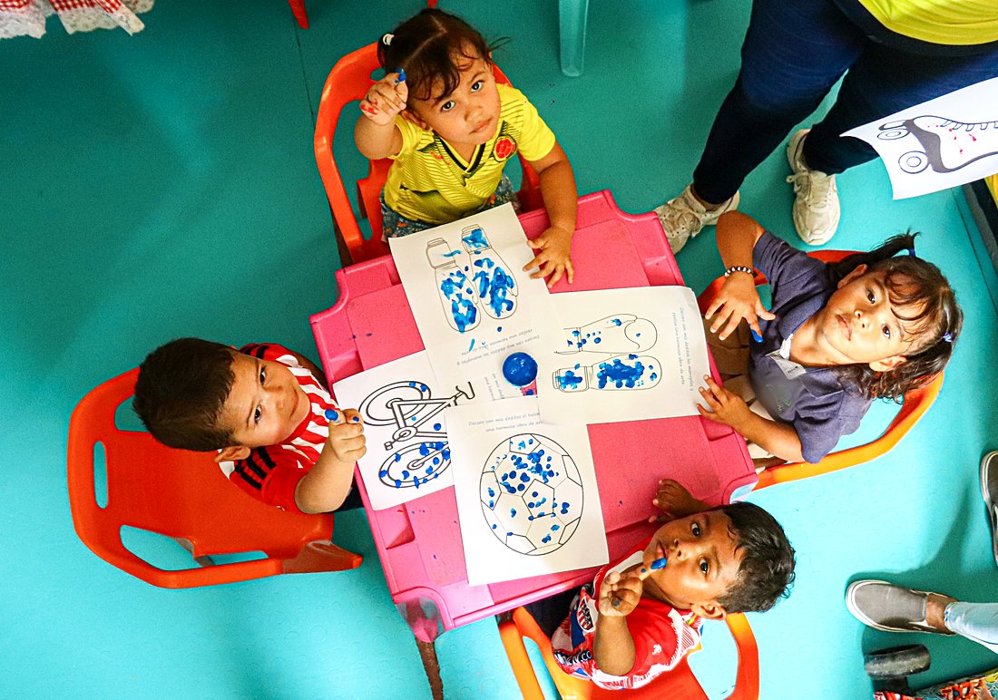 Niños pintando con los dedos alrededor de una mesa